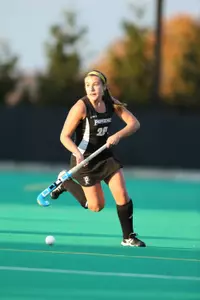 Field Hockey midfielder Emma Mackie controls the ball while running across the turf, looking up for an open pass.