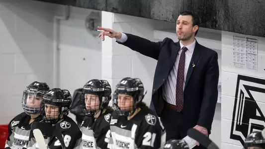 A photo of women's ice hockey head coach Matt Kelly coaching during a game behind the bench