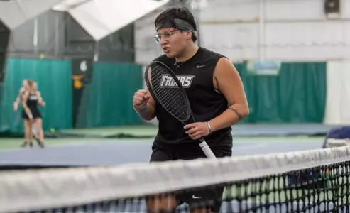 Tennis player Liria Loria celebrates a point near the net during a 2024 indoor match.