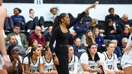 Erin Batth coaching on the sidelines of a game and pointing out directions to her team with a raised left hand holding a piece of paper