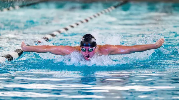 Quinn Danus surfaces above the water with black swim cap on swimming the butterfly stroke during dual meet competition.