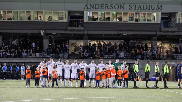 The men's soccer team stands together during the national anthem at Anderson Stadium.