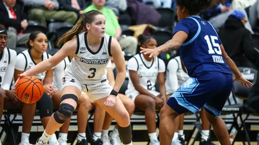 Orlagh Gormley dribbles the ball in front of the Providence College bench while being guarded by a Rhode Island defender.