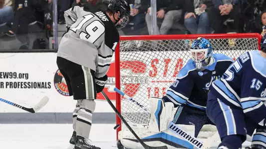 Providence College Ice Hockey player Tanner Adams looks to score from the crease as the Maine goalie defends the net.