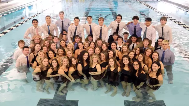 2025-26 Swimming and Diving Team posing for a group photo in the pool with the men's team dressed in shirt, tie and khakis pants, while the women are all in black dresses.