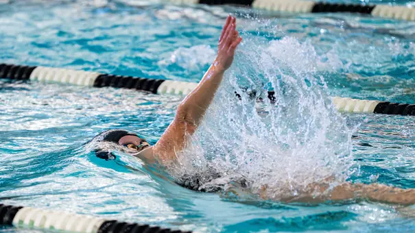 Bella Lombard raises her arm out of the water in a pool while competing in the backstroke.