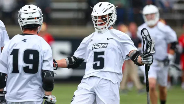 Rhett Chambers celebrates scoring a goal versus Denver with his arms out holding his stick with Chris Matia wearing white uniforms and white helmets with black trim.
