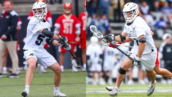 Rhett Chambers on the left side of the image winds up his lacrosse stick to shoot the ball in white uniform with white helmet on Chapey Field at Anderson Stadium. Jack Cooper on the right side of the image carries the ball on his stick after a faceoff win in white uniform with white helmet on Chapey Field at Anderson Stadium.
