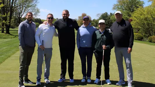 Men's Basketball Assistant Tee Butters and Head Coach Bryan Hodgson pose with four golfers on a tee box at a golf course during a Providence College Athletic Department fundraiser.