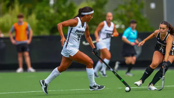 Bo Martina dribbles the ball with one hand using her field hockey stick.