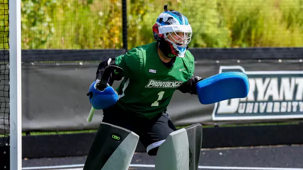 Friar goalkeeper Pauline Gineste, dressed in a green uniform with white trim and black goalie pads, crouches in a defensive stance in front of the goal.