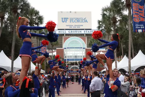 Cheerleaders in blue uniforms line up along Gator Walk with The Swamp in the background