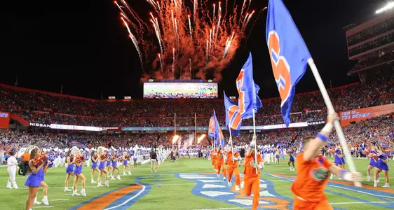 Cheerleaders with flags run out onto football field with fireworks in the background