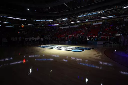 A spotlight shines on the March Madness center court logo inside a dark Lenovo Center in Raleigh before Florida's 2025 NCAA Tournament game vs. UConn.