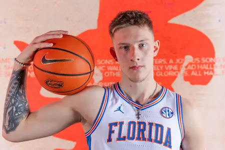 Arturas Butajevas poses in a white Florida basketball uniform with a basketball on his shoulder.