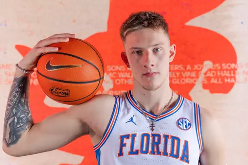 Arturas Butajevas poses in a white Florida basketball uniform with a basketball on his shoulder.