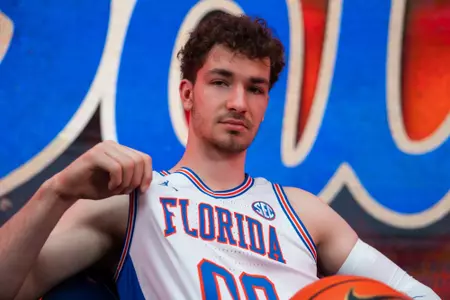 Domen Petrovic poses in a white uniform holding a basketball