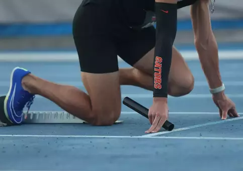 A male is in the starting blocks in a black uniform that says Gators