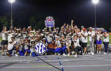 A group of men and women celebrate with a trophy in the dark under the lights