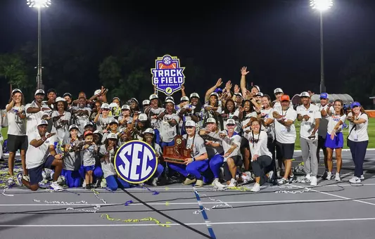 A group of men and women celebrate with a trophy in the dark under the lights
