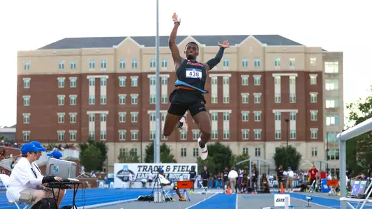 An athlete in a black uniform jumps over sand pit on gray day