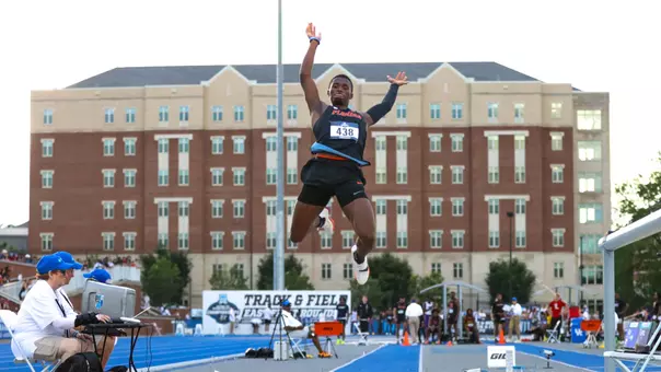 An athlete in a black uniform jumps over sand pit on gray day