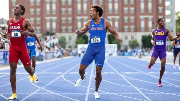A male in a blue Florida uniforms looks surprised as he runs on a track in front of a brick background