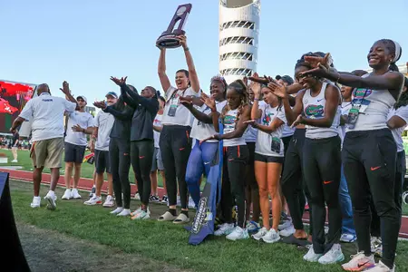 A group of women in white Florida Gators jerseys and black pants clap while a trophy is hoisted