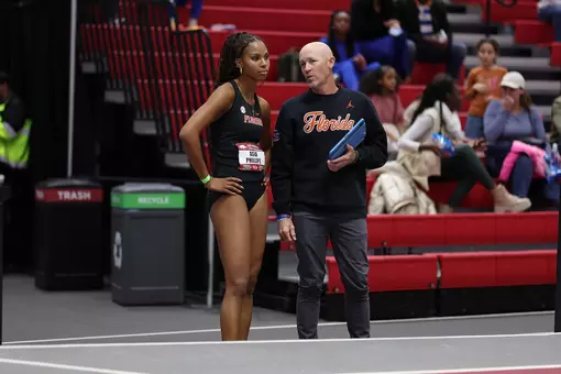 An athlete and coach both dressed in black having discussion at an indoor facility for track and field