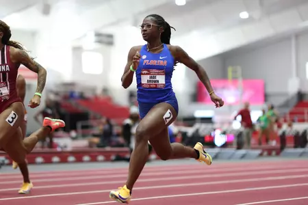 A female track athlete in a blue Florida uniform runs on a red track