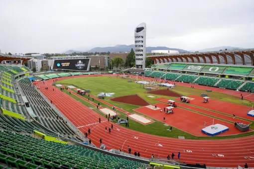 A green and orange stadium with a red track on a cloudy day with mountains in the background