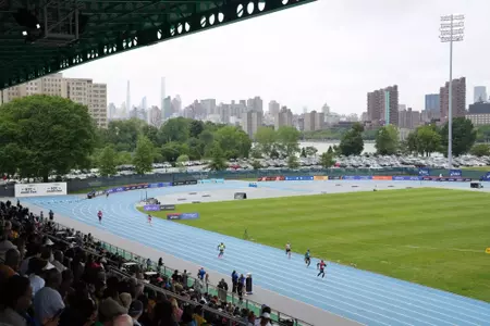 View from the top of a track and field stadium with a blue track on a cloudy day with city in background