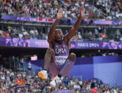 A male athlete in a Team USA uniform in the middle of a jump