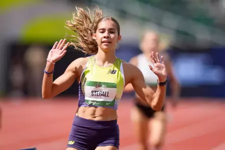 A female athlete in a bright yellow uniform places her hands in the air