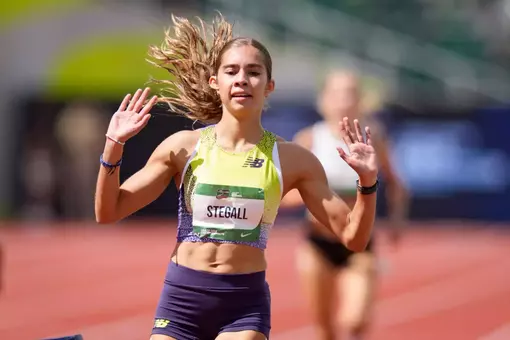 A female athlete in a bright yellow uniform places her hands in the air