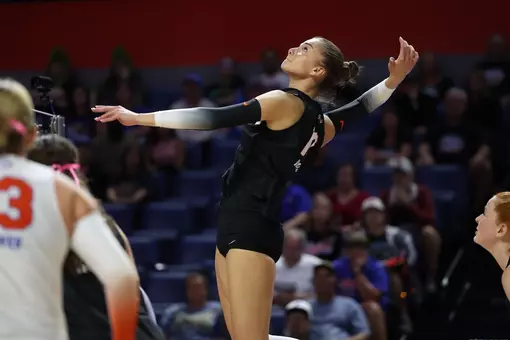 A female athlete in a black uniform spikes a volleyball