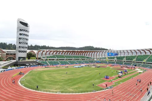 A track & field stadium with green seats and a tower on a cloudy day.