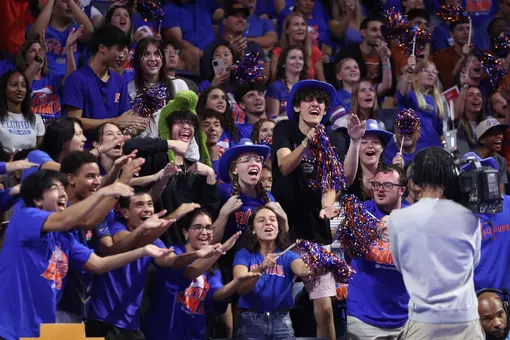 A group of fans in blue with clap and yell in front of tv camera