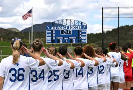 The women's soccer team salutes during the national anthem at Cadet Soccer Stadium