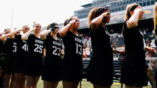 The women's lacrosse team salutes during the national anthem
