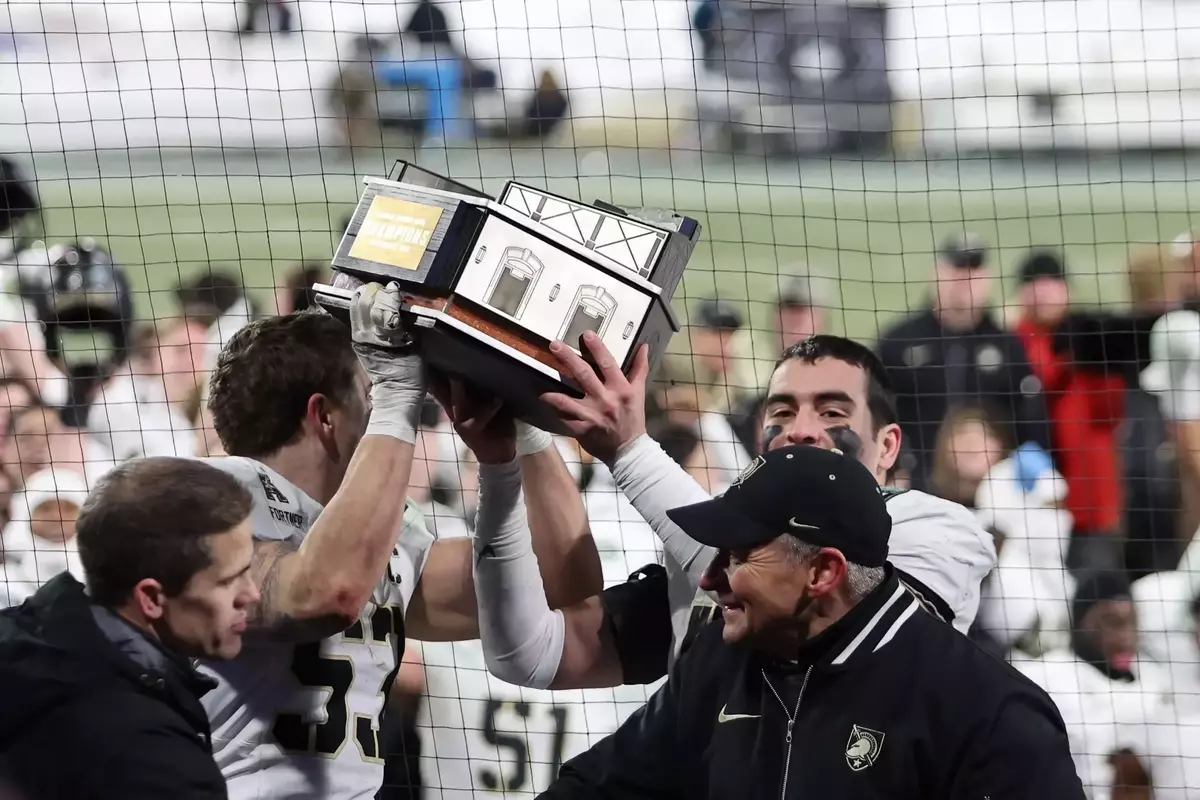 Army football captains Kalib Fortner and Andon Thomas lift the Fenway Bowl trophy at the first base dugout at Fenway Park.
