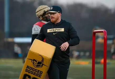 Assistant Coach Chandler Burks coaching at Spring Practice 2025 while holding a blocking pad.