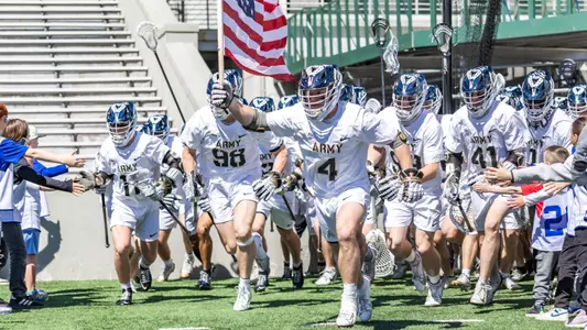 Evan Plunkett leads the men's lacrosse team onto the field holding the American flag.