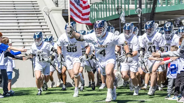 Evan Plunkett leads the men's lacrosse team onto the field holding the American flag.