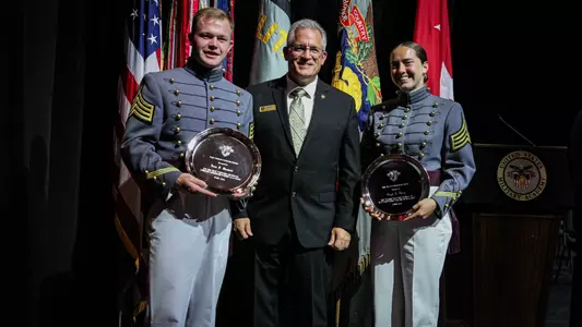 2026 AAA Award winners Evan Plunkett and Brigid Duffy hold their awards with Deputy Athletic Director Dan McCarthy on stage at the Superintendent's Award Convocation.