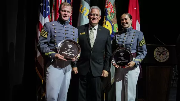 2026 AAA Award winners Evan Plunkett and Brigid Duffy hold their awards with Deputy Athletic Director Dan McCarthy on stage at the Superintendent's Award Convocation.