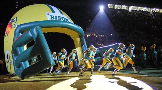 NDSU players are spotlighted running out of a helmet onto the football field.