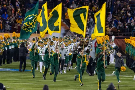 Cheerleaders carry flags spelling NDSU while running onto the field ahead of the NDSU football team.