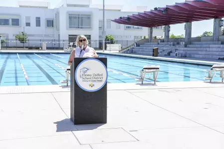 Jeanne Fleck, FUSD press conference, Fresno State Aquatics Center, pool in background, red roof above seating location with building in background