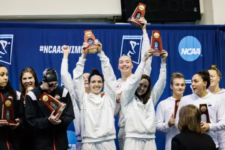The 200 medley relay team holds up their trophies on the podium